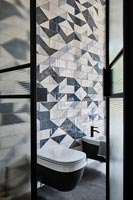 View into modern bathroom with patterned tiling on wall behind toilet 