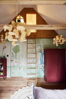 Ladder leading up to illuminated loft space in childrens bedroom 