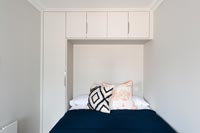 Small bedroom with built-in wardrobe and cupboards around bed 