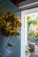 Wreath decorated with fairy lights on front door of country house 