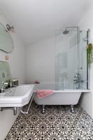 Monochrome bathroom with patterned flooring and roll top bath 