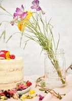 Cut flowers in a glass jar vase next to cake on table 