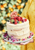Woman holding celebration cake covered in fruit and flowers 