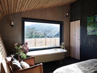 Bath next to window in modern wooden bedroom 