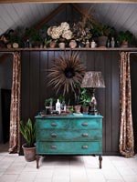 Teal painted chest of drawers against black wall 