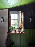Plants and decorations on windowsill of green and black painted bathroom 