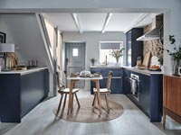 Small wooden dining table in centre of blue and white modern kitchen 