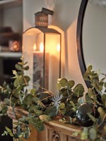 Lit candle in lantern with natural garland on mantelpiece at Christmas 