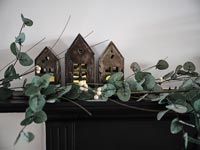 Garland of leaves with lanterns shaped as tiny houses on mantelpiece 