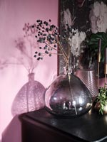 Black glass vase with seed heads against pink painted wall 