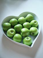 Heart shaped white fruit bowl filled with green apples 