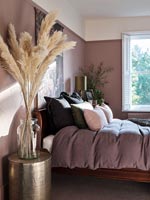 Ornamental grasses in vase in bedroom with dusky pink painted walls 