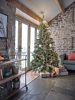 Christmas tree with gifts next to exposed brick wall  