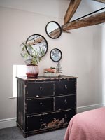 Black chest of drawers and display of round mirrors in country bedroom 