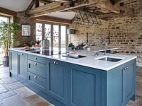 Modern blue kitchen with exposed wooden beams and stone wall 