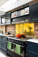 Exposed brick wall in modern kitchen with gold splashback panel 