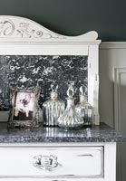 Decorative glassware on white painted chest of drawers with marble top