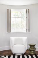 Modern white chair next to window with open shutters 