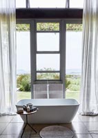 Freestanding bath next to large windows with scenic views of countryside 