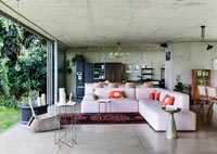 Corner sofa with kitchen and dining area with concrete walls and open bifolding doors to garden