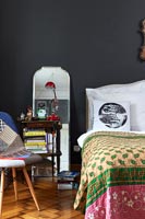 Mirror and bedside table in eclectic bedroom with black painted walls 