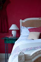 Rattan headboard against red painted wall in country bedroom 