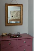 Gilded mirror over pink painted chest of drawers in bedroom 