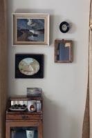 Display of framed pictures on wall above tiny wooden cabinet 