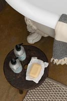 Soap and toiletries on small wooden table next to bath