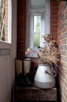Dried flowers in large metal urn and wellington boots in hallway