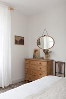 Vintage mirror above wooden chest of drawers in bedroom 