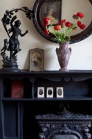 Red flowers in vase on black mantelpiece 