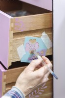 Woman using a stencil to add a subtle pattern on the sides of the drawers