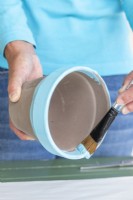 Using a brush to paint around the inside of the rim of the pot