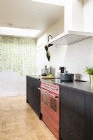 Modern country kitchen with dark cupboards, units, black wall lights, pink Aga and wooden floors