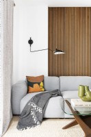 Contemporary living room with modular grey sofa, black arm wall light, mid-century coffee table and slatted wall, japandi style and cream rug