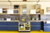 Modern retro kitchen with exposed brick, yellow rubber floor, blue cabinets, plywood, copper pipe lighting