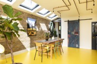 Modern retro kitchen with exposed brick, yellow rubber floor, blue cabinets, plywood, copper pipe lighting and upcycled table and chairs