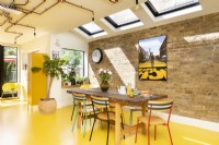Table and chairs in Modern retro kitchen with exposed brick, yellow rubber floor and copper pipe lighting