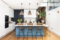 Modern contemporary kitchen in a side return extension with a blue island, pendants, wooden floors and bar stools