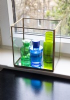 Blue and green glassware in glass box on windowsill - detail