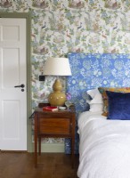Lamp on bedside table in classic bedroom with patterned wallpaper 