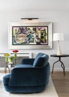 Living room with blue curved fabric sofa, round metal side tables with table lamp and painting, wall art.