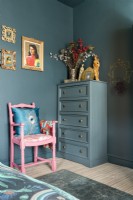 Painted tall boy chest of drawers in the corner of a bedroom with pink painted armchair