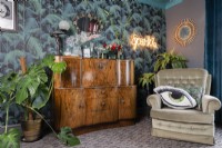 Wooden 1930's drinks cabinet and armchair and palm patterned wallpaper
