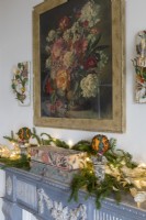 Mantlepiece decorated for christmas with painting of vase of flowers above
