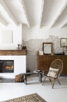 Wicker chair and old wooden sideboard next to lit fireplace