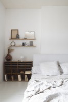 Wooden shelving unit next to bed in white country bedroom