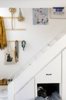White painted staircase with built-in storage and dog bed. Artwork and hooks hang on the wall.