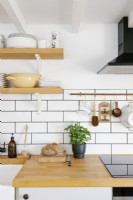 Contemporary L-shaped Kitchen with white subway tiles and wooden work surface. Wooden Shelving holds plates and crockery. 